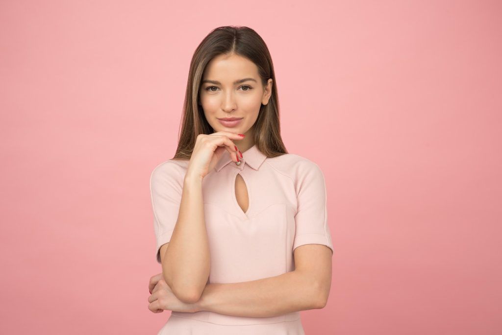 Woman against pink background with hand under chin