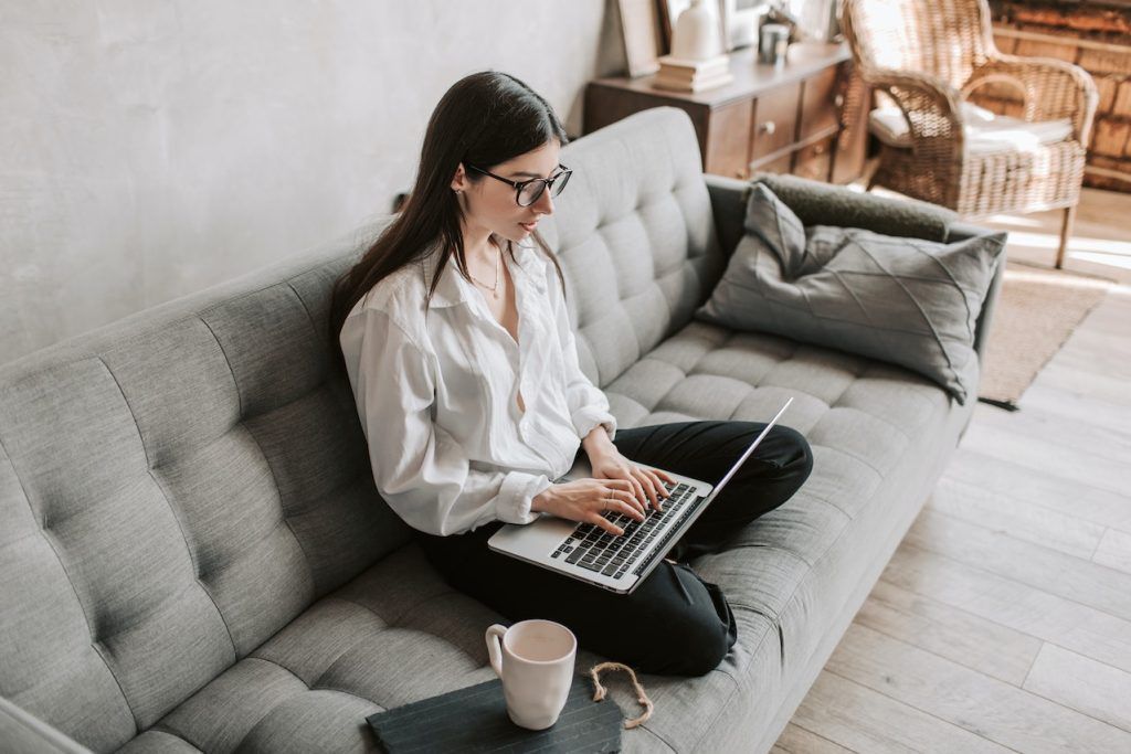 woman with glasses sitting on sofa using a laptop