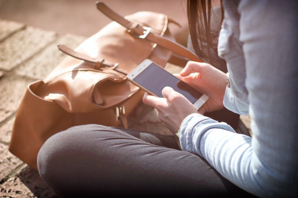 Woman sitting on her smartphone with her bag in front of her