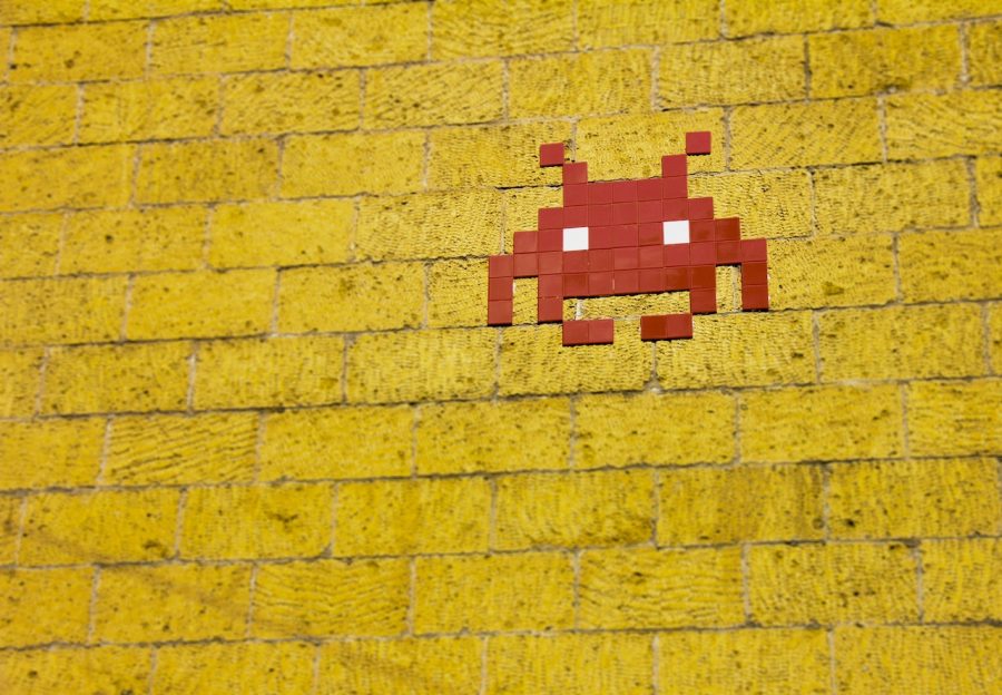 red Space Invaders pixel art on a yellow brick wall