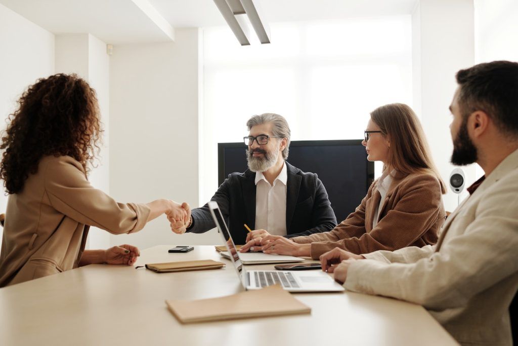 men and women in a boardroom, a man and woman are shaking hands