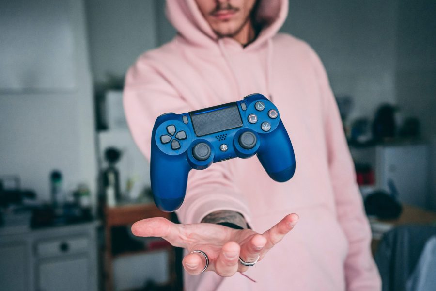 Man in pink hoodie tossing up a blue PlayStation 5 controller