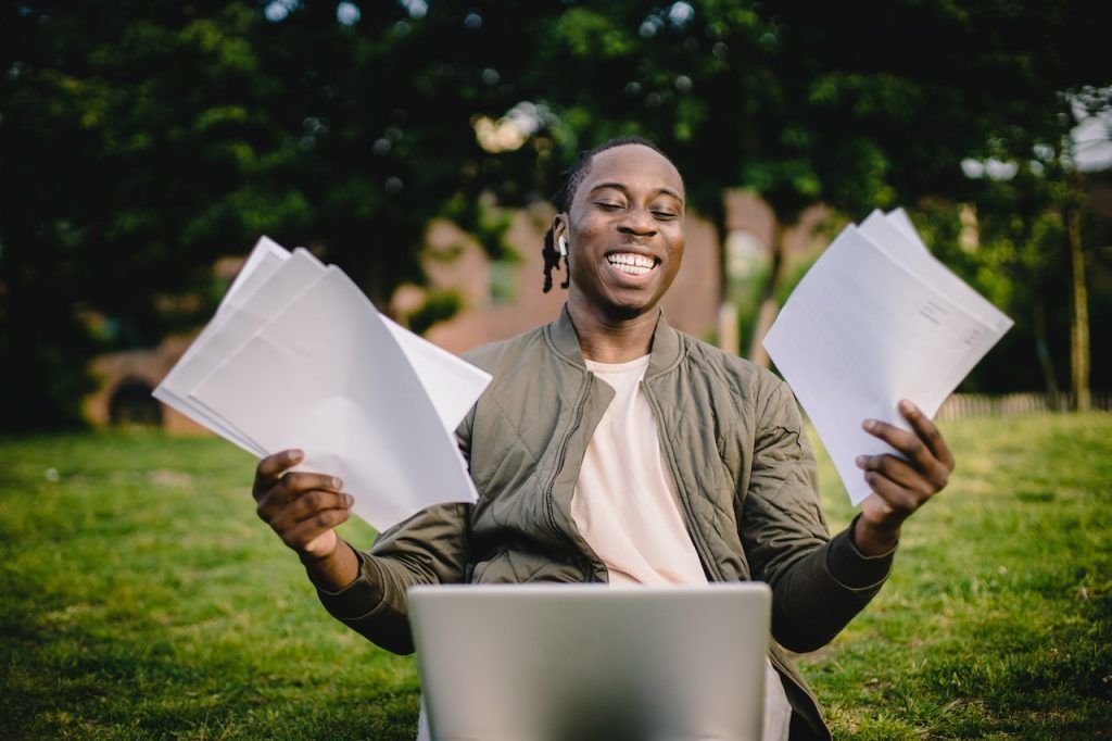 Happy man holding papers in front of his laptop outdoors