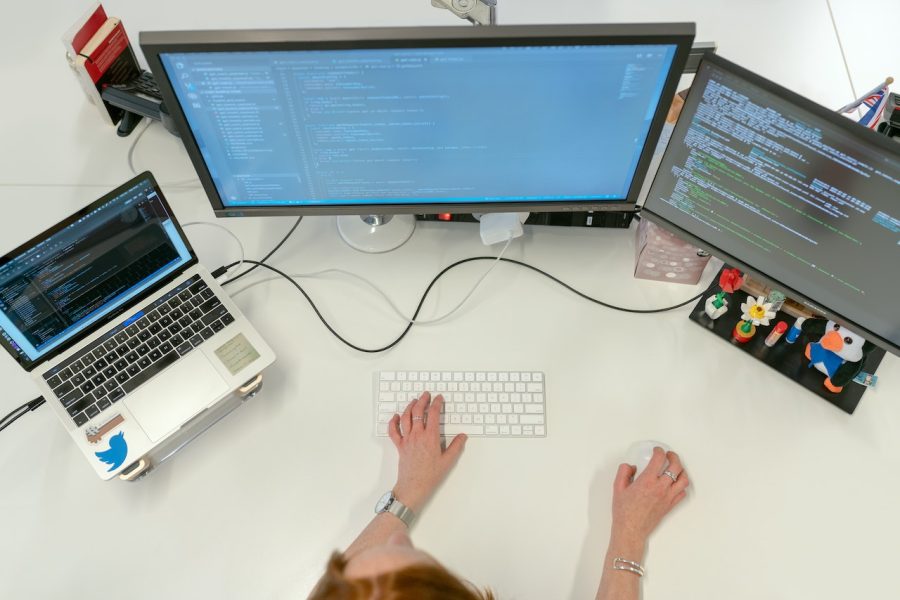 User's hands working a laptop with two additional monitors.