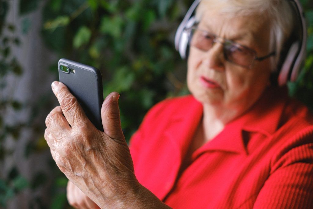 Old woman with over-the-ear headphones and a smartphone