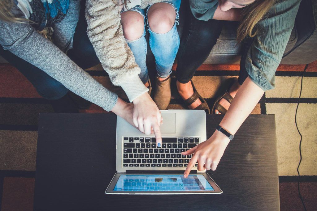 Three people looking at the screen of a silver laptop and pointing at it with their fingers.