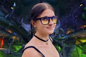 young woman wearing Gunnar World of Warcraft, Horde Edition Premium Gaming Glasses in front of a WoW Horde backdrop