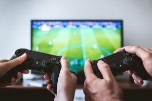 Close-up of two people's hands holding controllers in front of a TV