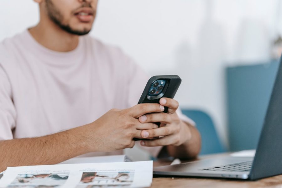 man using smartphone and laptop at desk