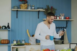 Man holding coffee cup and phone in kitchen