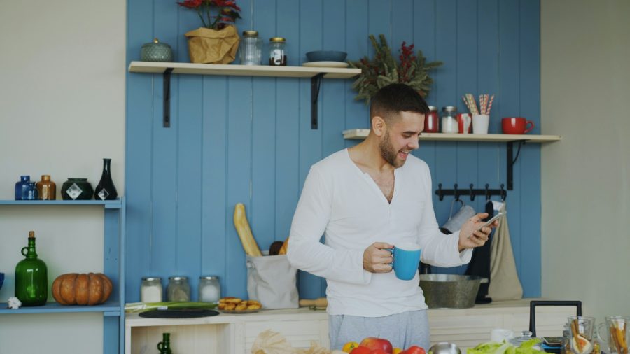Man holding coffee cup and phone in kitchen