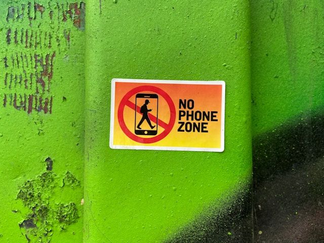 a no phone zone sign on a green wall