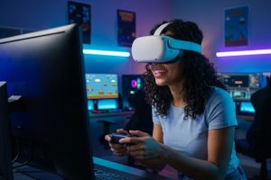 A photo of a smiling young woman wearing a virtual reality headset and holding a game controller, deeply engaged in a retro-style game. The setting is a dimly lit, modern home arcade room with vibrant neon blue and purple LED lighting, and a computer monitor showing the pixelated game interface.